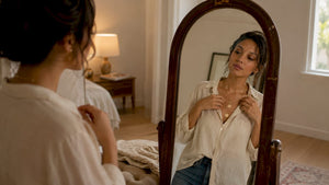 Woman adjusts layered gold necklaces in dressing room