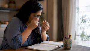 Woman inspecting gold pendant with loupe at home